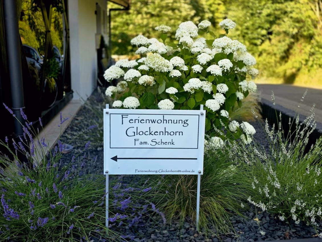 Schild „Ferienwohnung Glockenhorn – Fam. Schenk“ zwischen Hortensien und Lavendel